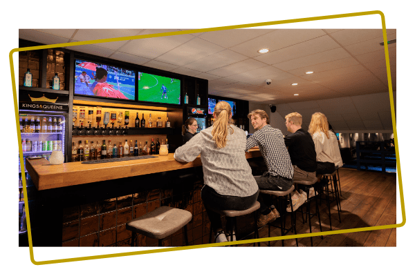 Bezoekers genieten van drankjes aan de bar in de sportsbar van Kings & Queens in Assen